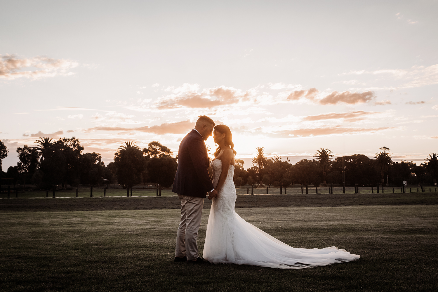 Natural golden hour portrait of a bride and groom embracing in a grassy field. A romantic capture of the moment during a hazy, warm sunset, typical of Melbourne and Mornington Peninsula weddings