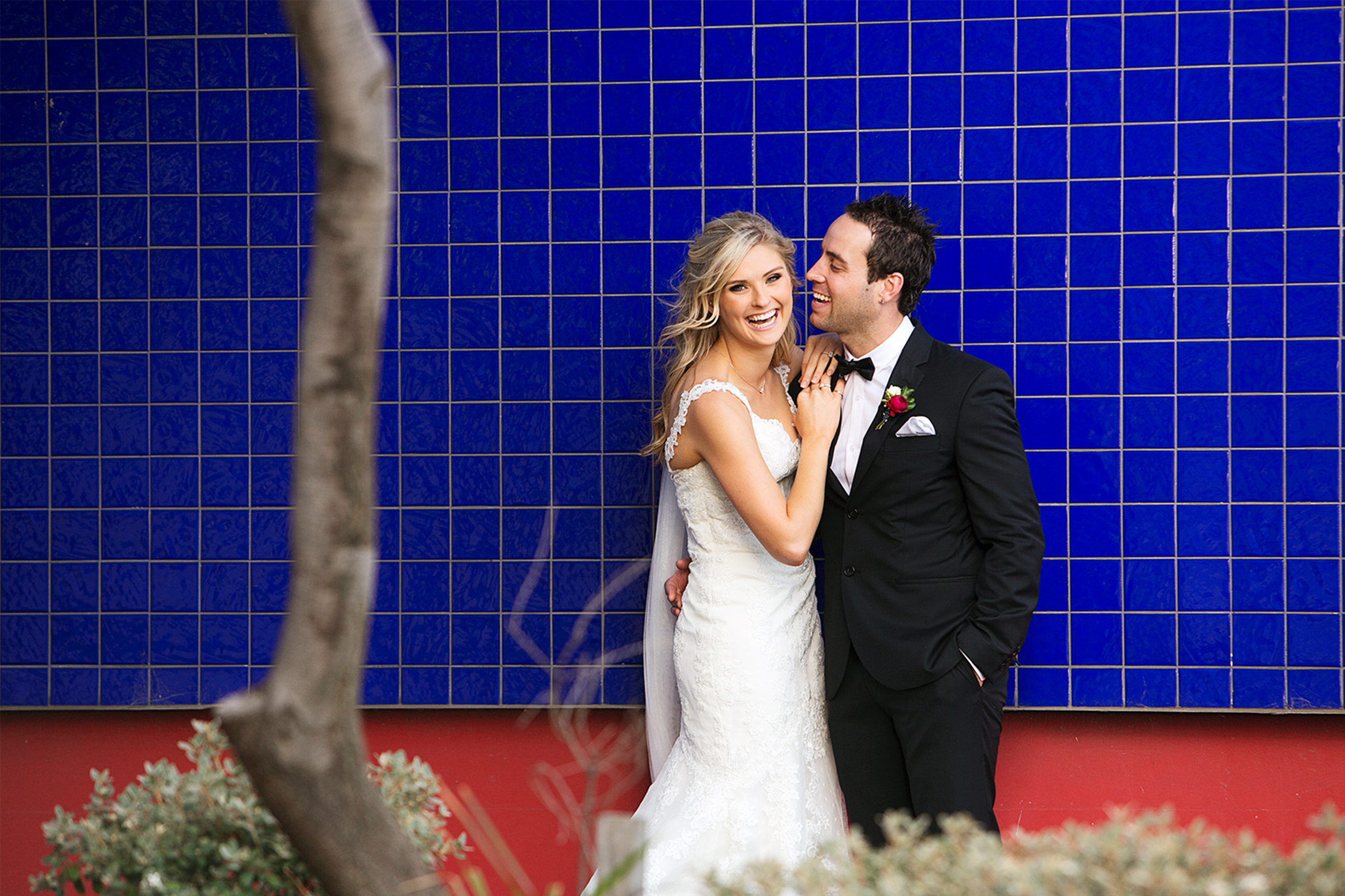 Candid wedding photo of bride and groom laughing together against vibrant blue tiled wall, natural fun wedding photography Melbourne, Yarra Valley, Mornington Peninsula