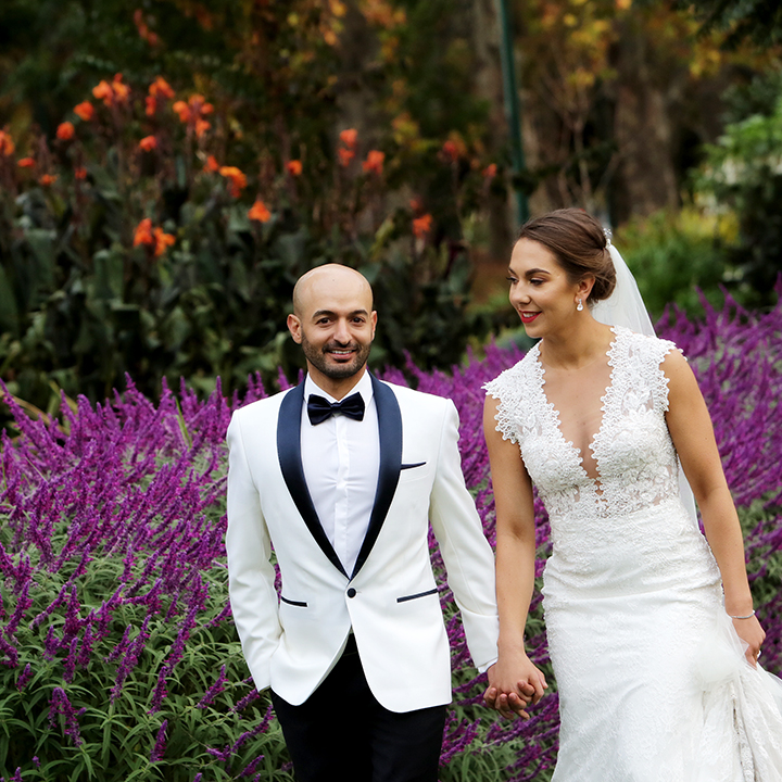 Candid wedding photo of bride and groom walking hand-in-hand through vibrant garden with purple flowers, natural fun wedding photography Melbourne, Yarra Valley, Mornington Peninsula